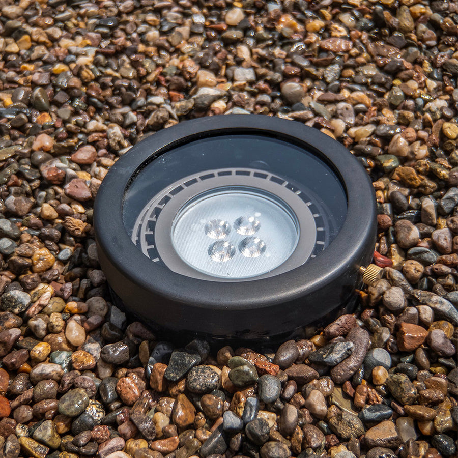 Brilliance black flat-top PAR36 well light installed in gravel with lamp visible through the glass lens